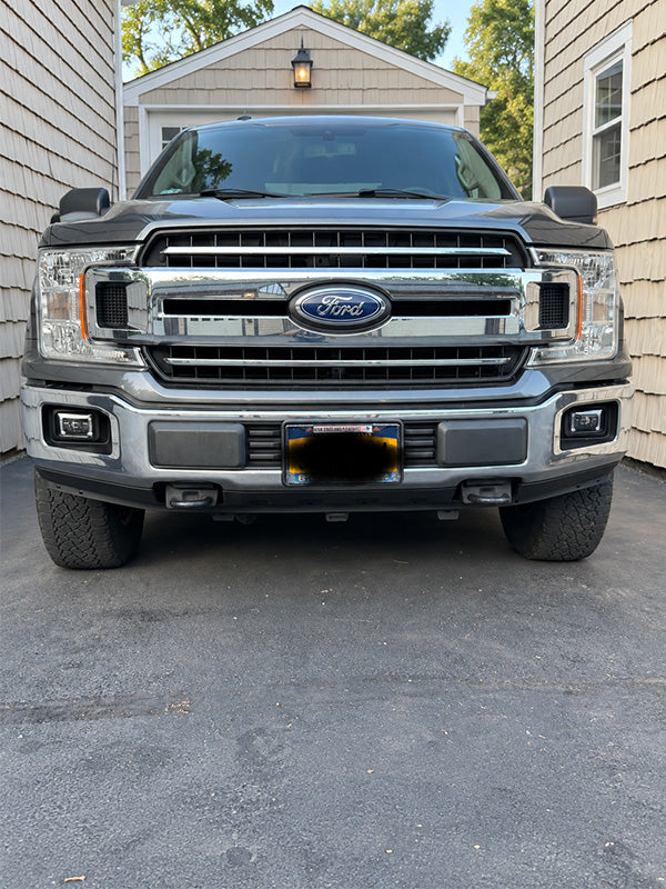 Front view of a dark gray Ford pickup truck parked in a driveway between beige houses.