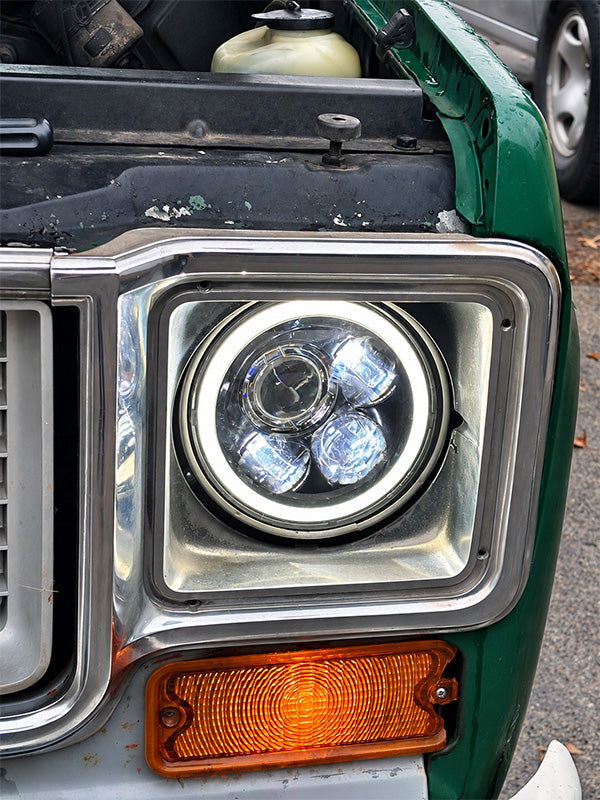 Close-up of a vintage green vehicle headlight with a chrome bezel, dual circular bulbs, and an amber side marker light, parked outdoors.