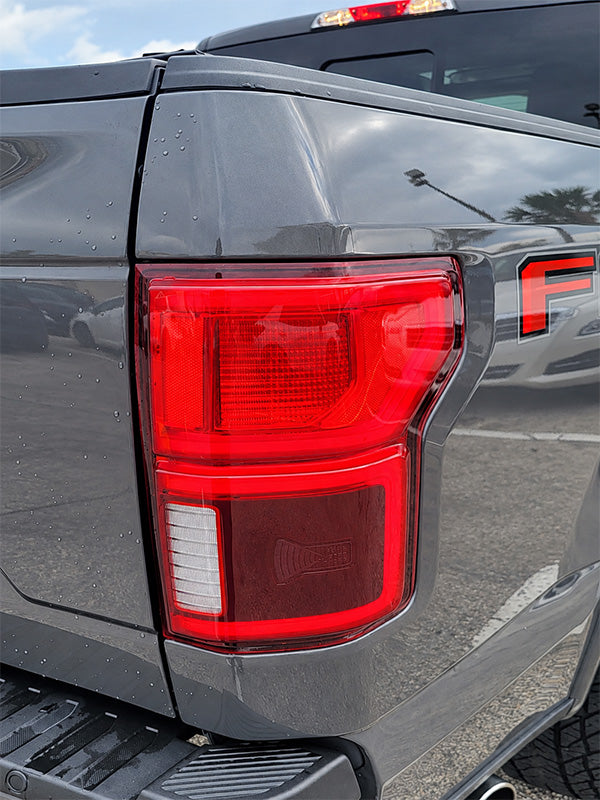 Close-up of the rear left taillight of a dark gray pickup truck, showing the red LED light assembly and part of the truck body.