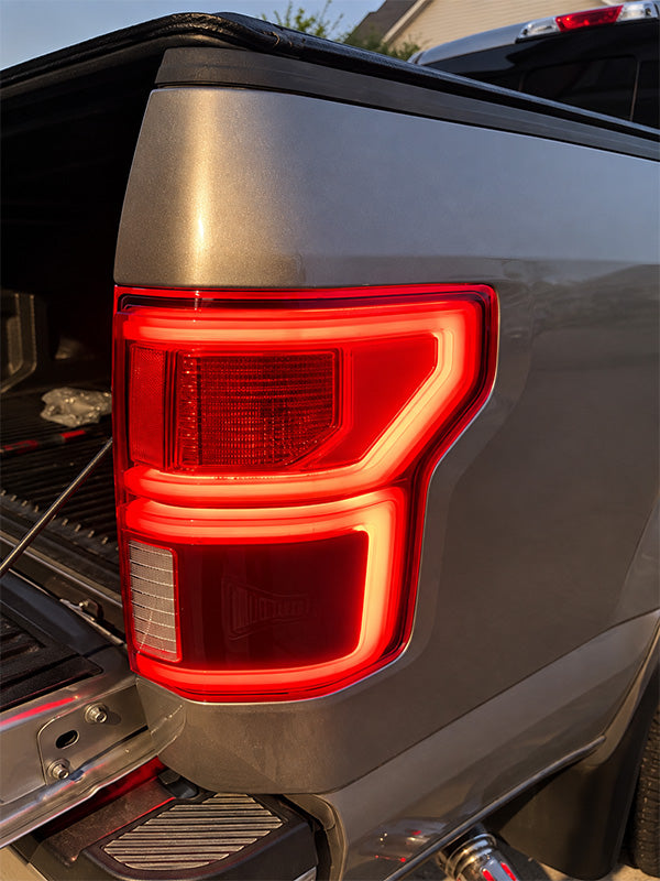Close-up of the rear left taillight of a dark gray pickup truck, showing the illuminated red LED light bar and clear lens sections.