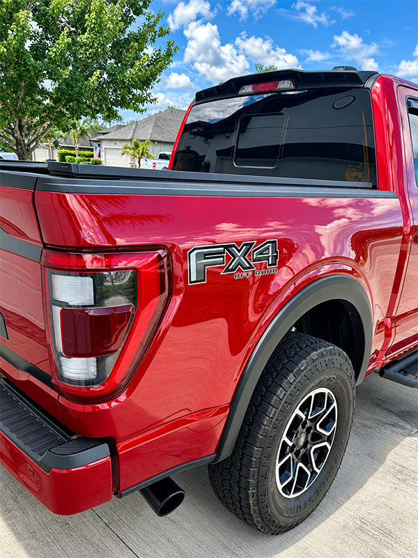 Close-up rear three-quarter view of a red Ford F-45 FX4 pickup truck parked outdoors on a paved surface under a blue sky with clouds. The FX4 badge is visible on the rear quarter panel.
