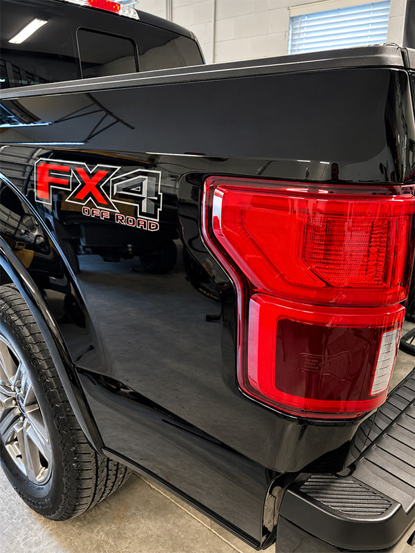 Close-up of the rear left side of a black pickup truck in a garage, showing the FX4 Off Road badge, red taillight, rear wheel, and step bumper.