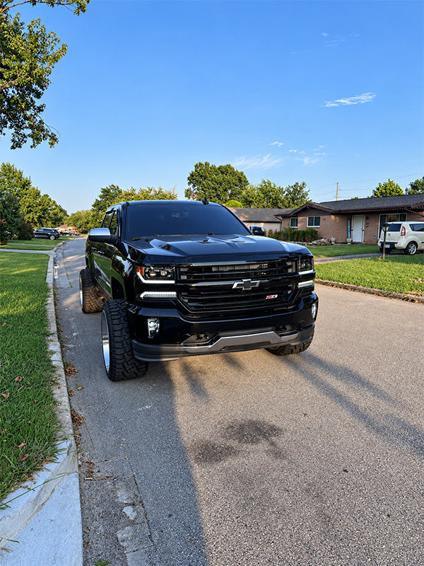 A black lifted Chevrolet Silverado pickup truck parked on a residential street under a blue sky.