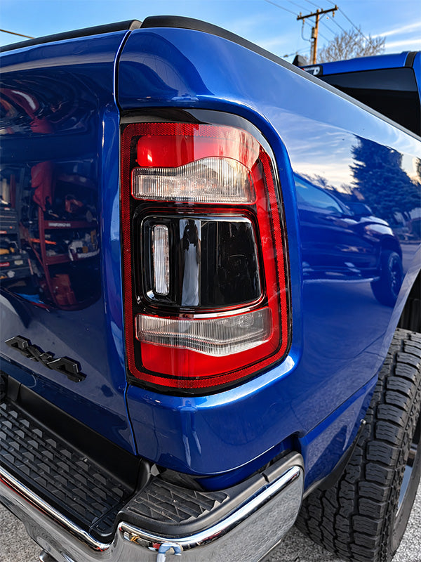 Close-up of the rear left side of a bright blue pickup truck, showing the taillight, rear bumper, tire, and a small black V8 badge.