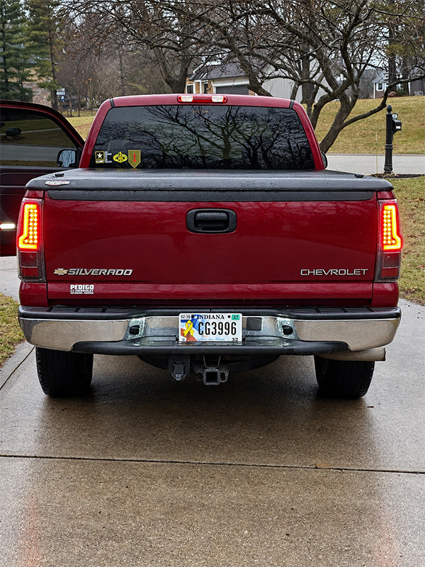 Rear view of a red Chevrolet Silverado pickup truck parked on a wet concrete driveway, with trees and houses in the background.