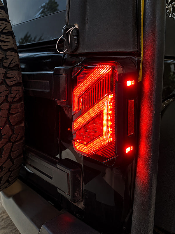 Close-up of a black vehicle rear corner with a glowing red LED taillight and small side marker lights, mounted on a black body panel.
