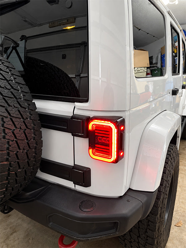 A close-up of a white vehicle's rear side showing a custom red LED light bar mounted between the rear doors, with a spare tire on the left side.