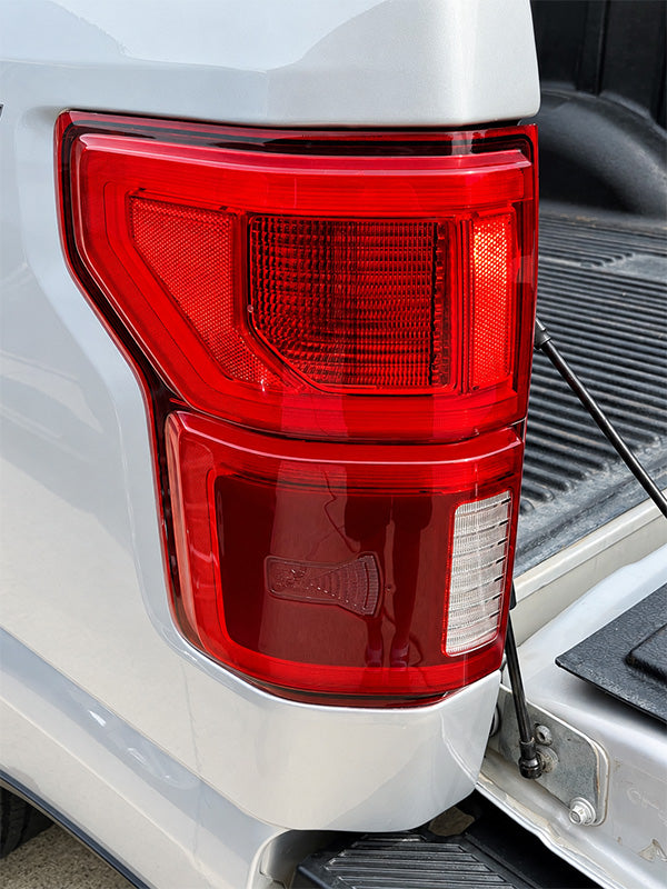Close-up of a white pickup truck's rear left taillight assembly, showing the red lens, white reflector, and part of the open truck bed.